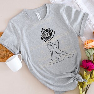 May include: A gray t-shirt with a black line drawing of a person sitting with their head in their hands. The drawing is stylized and abstract. The person's head is replaced with a circle with a line through it.