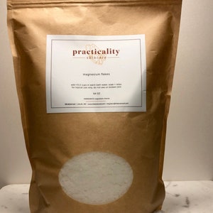 May include: A brown paper bag of magnesium flakes from Practicality Skincare. The bag has a clear window showing the white flakes. The label reads "magnesium flakes" and provides usage instructions. The bag contains 64 oz of product.
