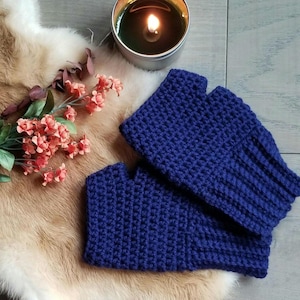 May include: A pair of blue crocheted fingerless gloves. The gloves are made with a simple stitch pattern and have a ribbed cuff.