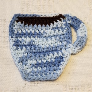 May include: A crocheted blue and white coffee cup coaster with a brown crocheted rim.