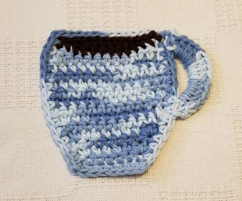 May include: A crocheted blue and white coffee cup coaster with a brown crocheted rim.