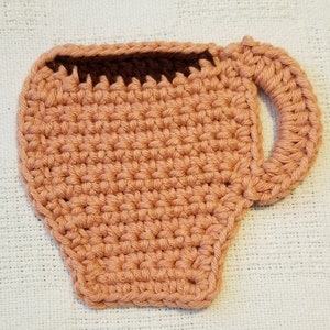 May include: A crocheted coffee cup coaster in a peach colour with a brown crocheted rim.