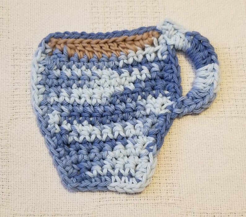 May include: A crocheted blue and white cup coaster with a brown rim. The coaster is shaped like a cup with a handle.