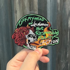 May include: A black embroidered patch with a skull and flames. The text reads "Off my head on laudanum Not responsible for my action".