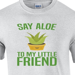 May include: A gray t-shirt with the text "Say Aloe to my little friend" in green letters. A cartoon aloe plant with a smiley face is in the middle of the text.