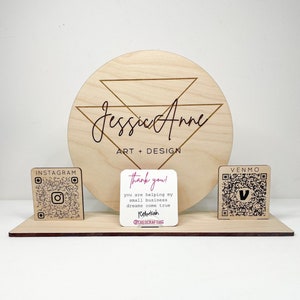 May include: A wooden sign with the text "Jessie Anne Art + Design" in a cursive font. The sign is decorated with a geometric design and includes QR codes for Instagram and Venmo. A small card with the text "Thank you! You are helping my small business dreams come true. Rebekah @CREOCRAFTING" is also included.