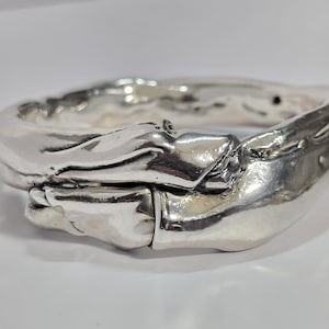 May include: A silver bracelet with a unique, organic design. The bracelet is made of two pieces that are intertwined and have a textured surface.