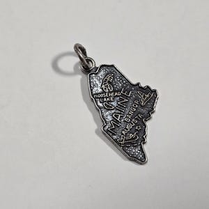 May include: Silver charm shaped like the state of Maine with the word "Maine" and the names of cities including "Moosehead Lake", "Bangor", and "Augusta" written on it.