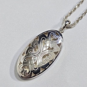May include: Silver oval pendant with an openwork design. The pendant hangs from a silver rope chain. The intricate pattern features swirling lines and heart-shaped cutouts. The jewelry is displayed on a white surface.