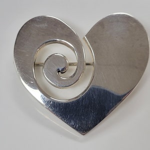May include: A silver heart-shaped brooch with a swirling design in the centre.