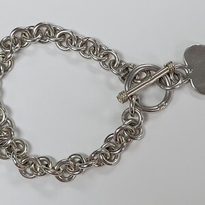 Könnte beinhalten: Ein silbernes Kettenarmband mit einem herzförmigen Anhänger und einem Schiebeverschluss.