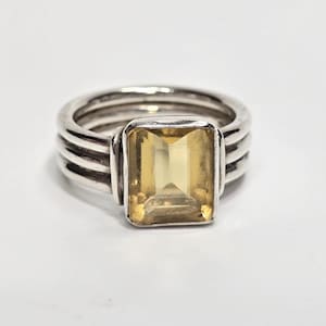 May include: A silver ring featuring a rectangular, emerald-cut yellow gemstone set in the center. The band is constructed from three parallel silver wires that merge together at the base, creating a layered, multi-band appearance around the finger.