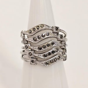 May include: A silver ring with multiple bands set with small black diamonds. The bands are stacked and form a wavy pattern.
