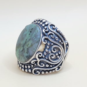 Op de afbeelding: Een zilveren ring met een groene steen in een decoratief filigraanontwerp.