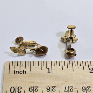 May include: A pair of vintage gold-toned clip-on earrings. Each earring features a leaf design and a brown, oval-shaped stone. The earrings are approximately 1 inch in length.
