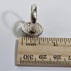 Puede incluir: Anillo de plata con una cara redonda con un dise&ntilde;o de coraz&oacute;n. El anillo est&aacute; junto a una regla que muestra medidas en pulgadas. La cara del anillo tiene aproximadamente 1,3 cm de di&aacute;metro.