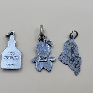 May include: Three silver charm pendants. The first is a church with the text "I am a Presbyterian" and "Dayware Co. Sterling". The second is a girl with the text "Mexico 925" on the back. The third is a state outline with the text "Sterling" on the back.