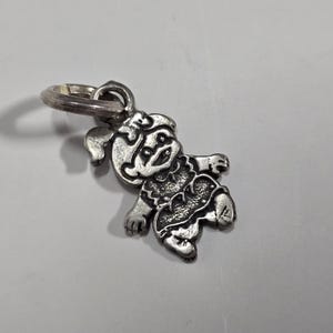 May include: A silver charm featuring a cartoon girl with a bow in her hair. The charm is attached to a silver ring.