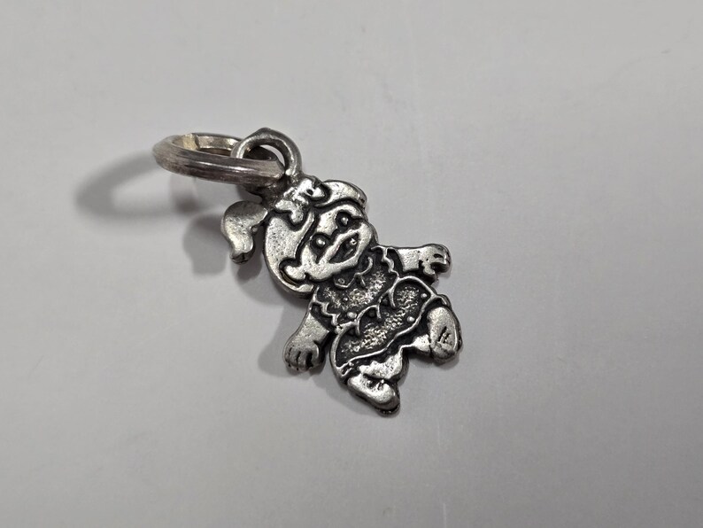 May include: A silver charm featuring a cartoon girl with a bow in her hair. The charm is attached to a silver ring.