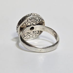 Puede incluir: Un anillo de plata con una cara grande y redonda. La cara del anillo est&aacute; decorada con recortes en forma de coraz&oacute;n y patrones arremolinados. La banda es lisa y pulida. El anillo est&aacute; sobre un fondo blanco.