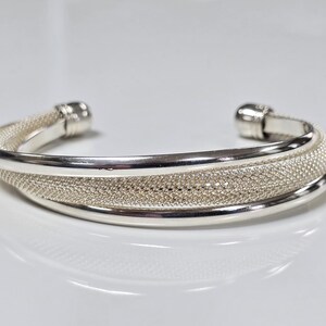 Peut inclure: Un bracelet en argent avec un motif texturé et tissé. Le bracelet est ouvert et possède un fermoir à charnière.