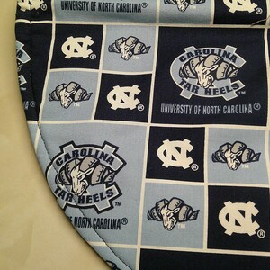 May include: A fabric item featuring a grid pattern of navy blue and light blue squares. The design includes the University of North Carolina logo, the Carolina Tar Heels ram mascot, and the text University of North Carolina and Carolina Tar Heels.