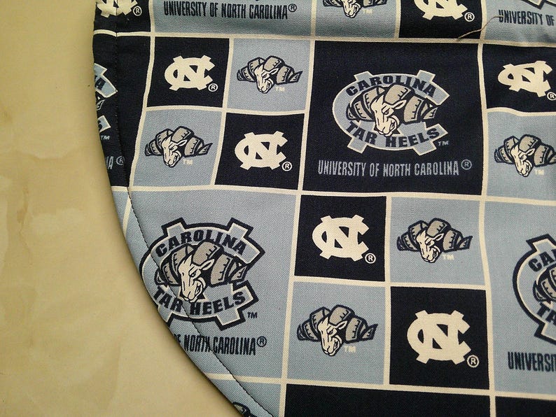 May include: A fabric item featuring a grid pattern of navy blue and light blue squares. The design includes the University of North Carolina logo, the Carolina Tar Heels ram mascot, and the text University of North Carolina and Carolina Tar Heels.