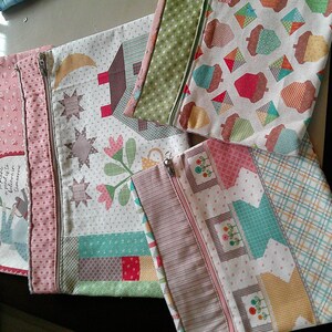 May include: Three rectangular fabric zipper pouches featuring patchwork designs. One pouch displays a person gardening with the text 'To plant a garden is to believe in tomorrow'. Others feature patterns of acorns, houses, flowers, and plaid.