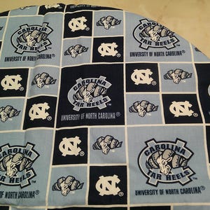 May include: A fabric featuring a repeating grid pattern of light blue and dark navy squares. The design includes the University of North Carolina Tar Heels logo, the ram mascot head, and the text Carolina Tar Heels University of North Carolina.