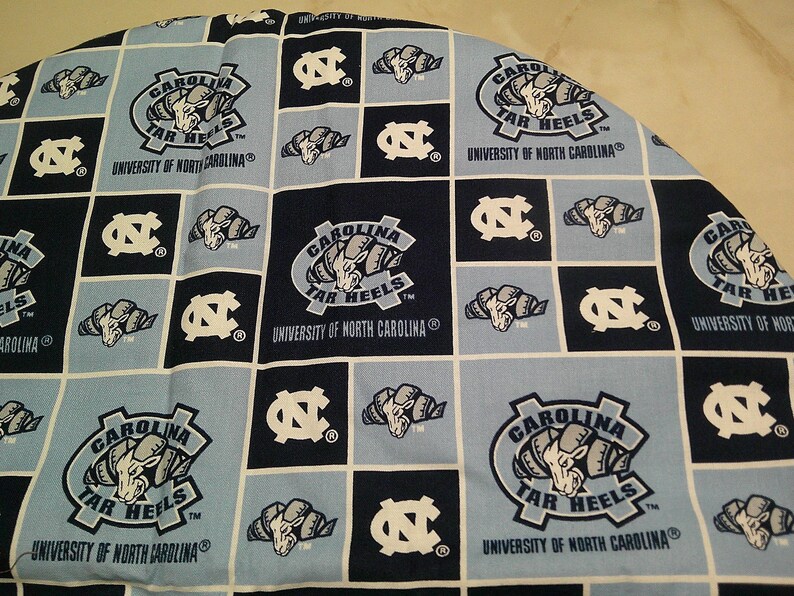 May include: A fabric featuring a repeating grid pattern of light blue and dark navy squares. The design includes the University of North Carolina Tar Heels logo, the ram mascot head, and the text Carolina Tar Heels University of North Carolina.