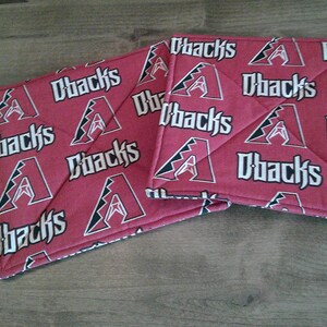May include: Two square fabric pot holders featuring a repeating pattern of the Arizona Diamondbacks logo and the text Dbacks in white and black on a red background. The quilted fabric items have stitched diagonal lines across the surface.
