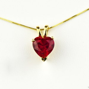 Peut inclure: Un collier en chaîne dorée avec un pendentif en forme de cœur orné d'une pierre précieuse rouge.