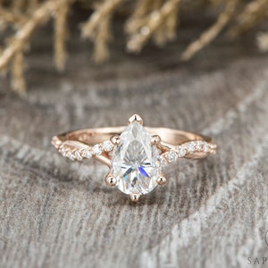 Puede incluir: Un anillo de compromiso de diamante de forma pera engastado en oro rosa con una banda retorcida y diamantes más pequeños en la banda.