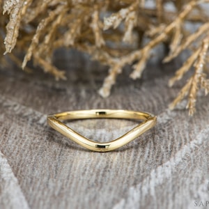May include: A simple gold wedding band with a curved, V-shaped design.