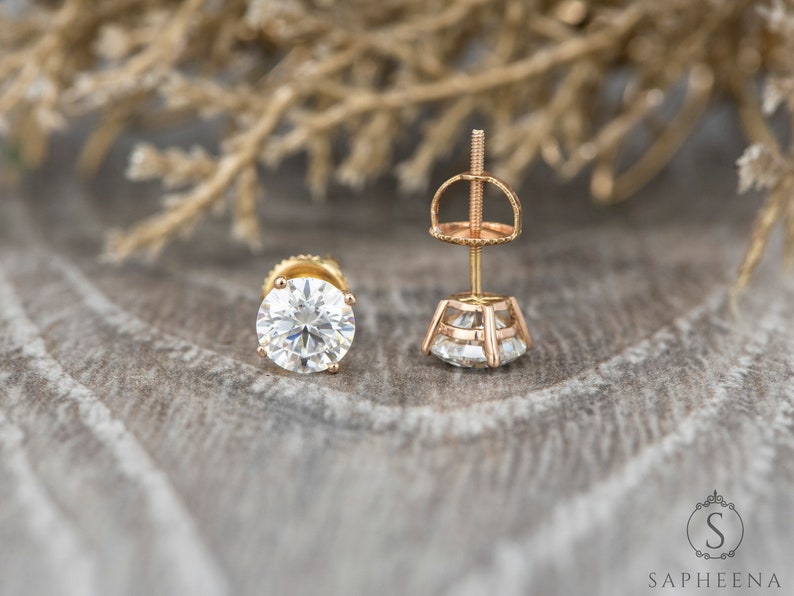 May include: A pair of gold stud earrings with a round, clear gemstone. The earrings have a screw-back closure.