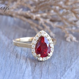 May include: A gold ring with a pear-shaped red gemstone surrounded by a halo of smaller white gemstones.