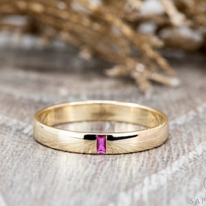 May include: A gold band ring with a single, small, rectangular pink gemstone set in the centre.