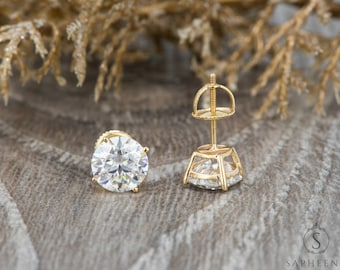 May include: A pair of gold stud earrings with a large, round, clear gemstone. The earrings are set in a prong setting and have a screw-back closure.
