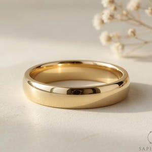 Peut inclure: Une alliance en or poli. La bague est présentée sur un fond neutre avec un éclairage doux. La conception classique de la bague est idéale pour un mariage ou des fiançailles.