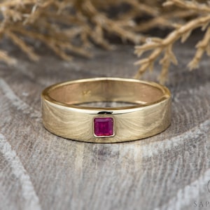 May include: A gold band ring with a square-shaped ruby gemstone set in the center.