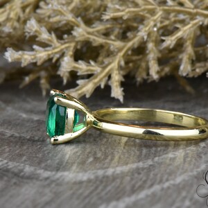 Op de afbeelding: Een gouden ring met een grote, smaragdgroene edelsteen in een kraalbezetting. De ring ligt op een houten oppervlak.