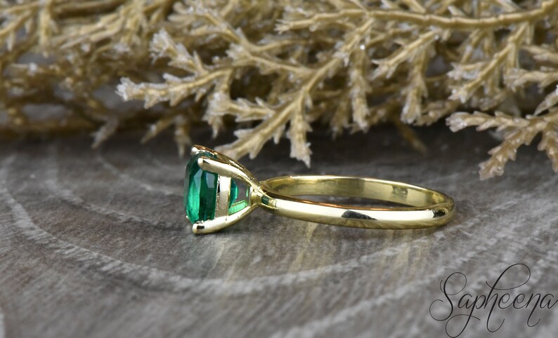 Op de afbeelding: Een gouden ring met een grote, smaragdgroene edelsteen in een kraalbezetting. De ring ligt op een houten oppervlak.