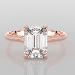 May include: A rose gold engagement ring with a large, clear emerald cut diamond.