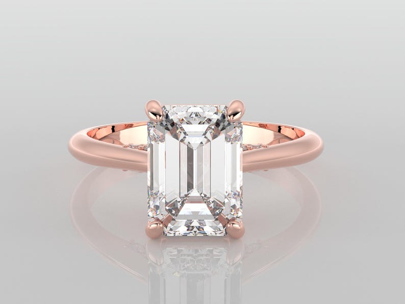 May include: A rose gold engagement ring with a large, clear emerald cut diamond.