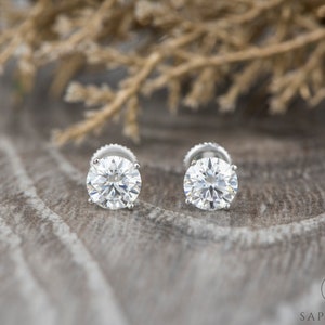 May include: A pair of round, clear diamond stud earrings set in silver.