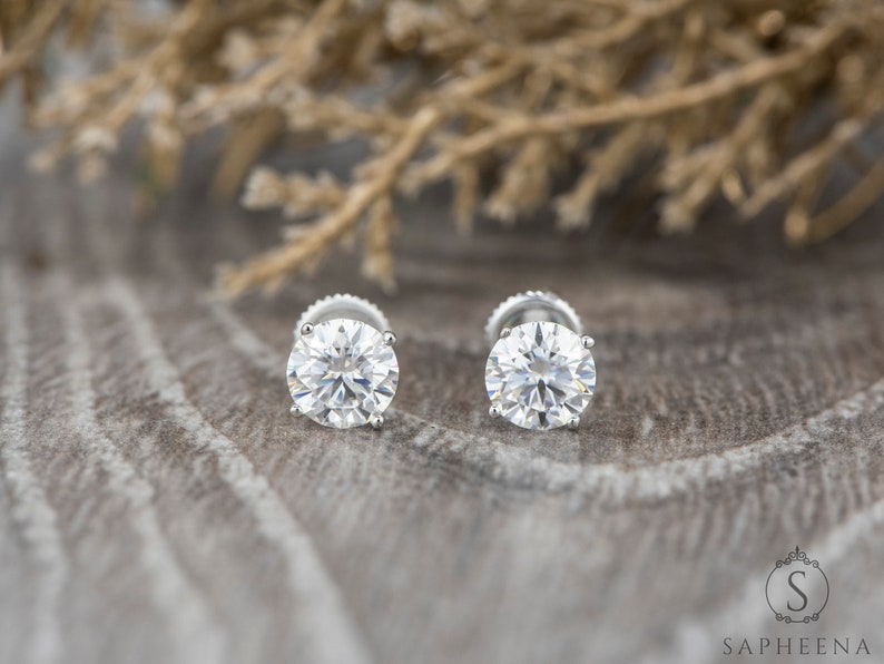 May include: A pair of round, clear diamond stud earrings set in silver.