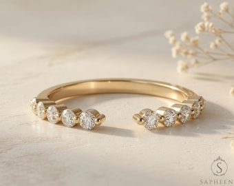 May include: A gold-colored ring with a row of clear, round gemstones. The ring has an open design, with the gemstones set along the top half of the band. The ring is displayed on a light-colored surface.