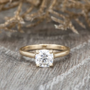 May include: A gold solitaire engagement ring with a round brilliant cut diamond.