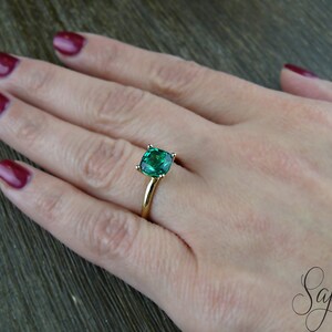 Op de afbeelding: Een gouden ring met een grote, vierkante smaragdgroene edelsteen.