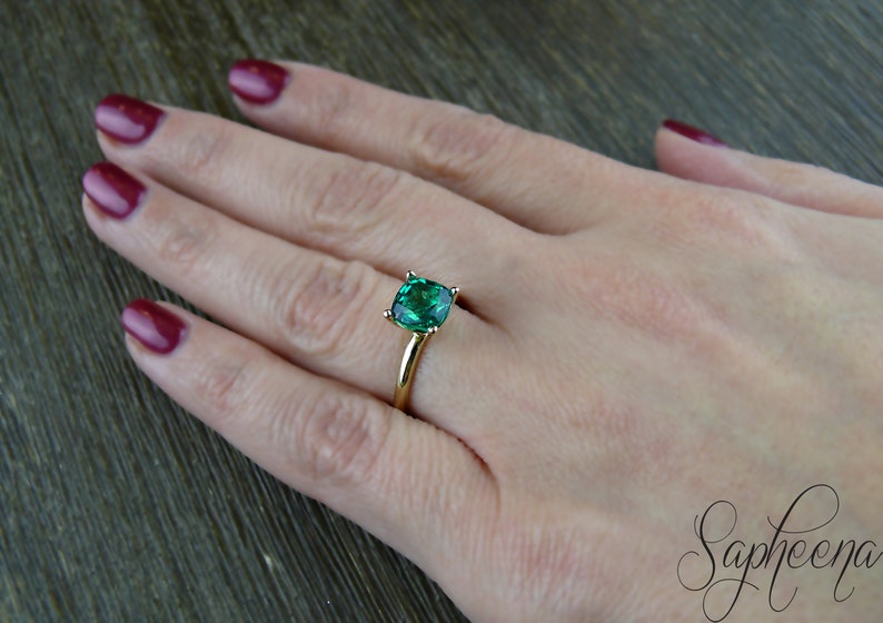 Op de afbeelding: Een gouden ring met een grote, vierkante smaragdgroene edelsteen.